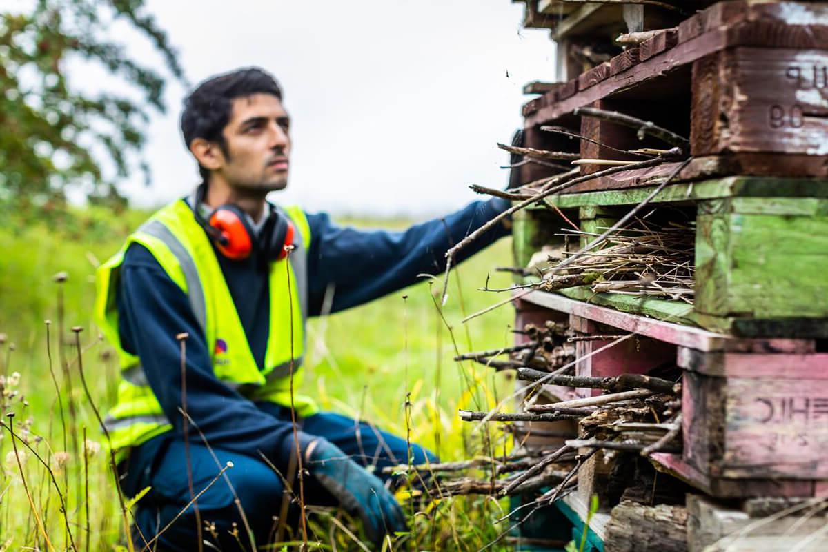 Mitie employee in high vis kneeling by a pile of old wooden pallets and sticks, created for wildlife